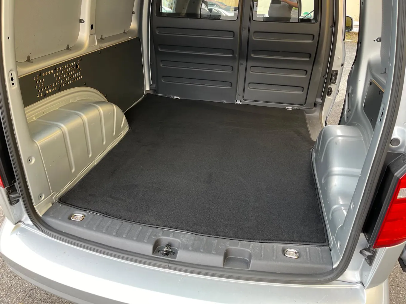 Blick durch die Hintertür in den Laderaum eines VW Caddy, dessen Boden mit einer schwarzen Laderaumschutzmatte verkleidet ist.