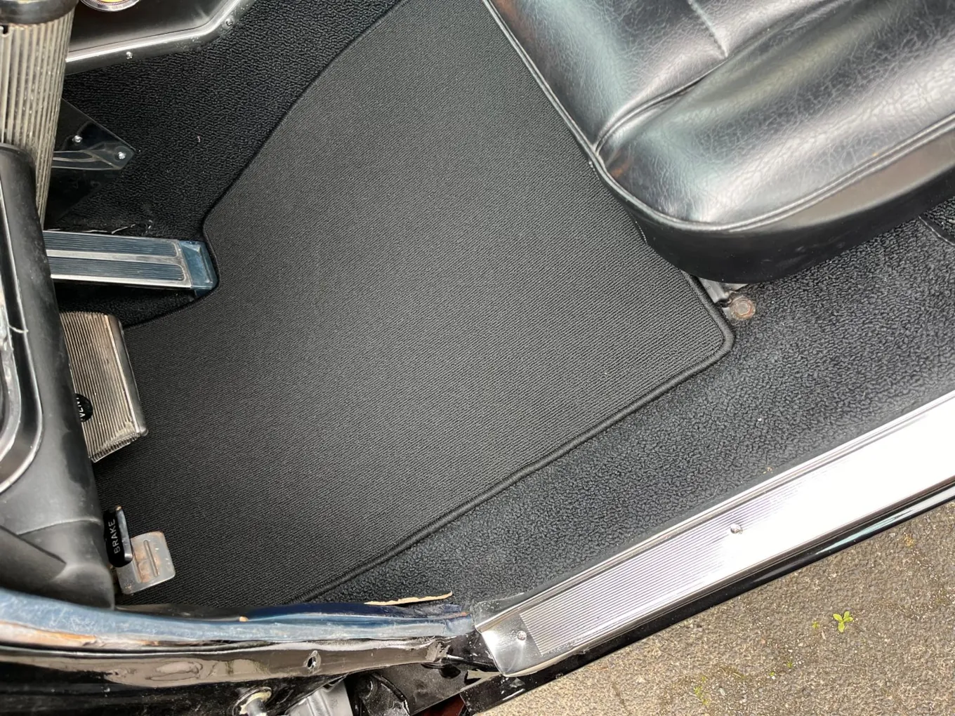 Blick in den Fahrerfußraum eines Buick Riviera 1964. Dort liegt eine graue Fußmatte.