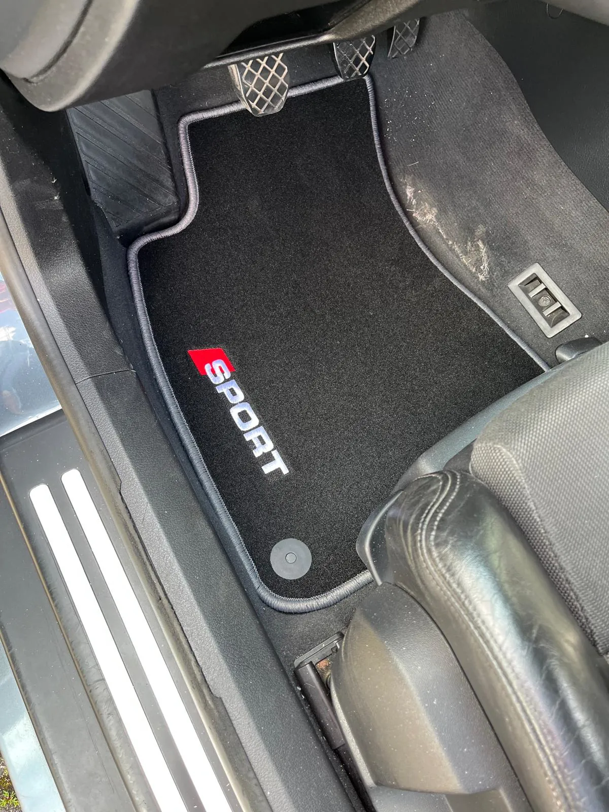 Blick in den Fahrerfußraum eines Audi A4 8H Cabriolets. Hier liegt eine Fußmatte mit dem Stick "Sport".