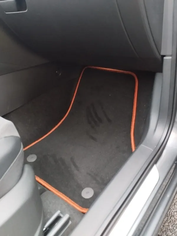 Blick in den Beifahrerfußraum eines Cupra Ateca, in dem eine schwarze Fußmatte mit rotem Rand liegt.