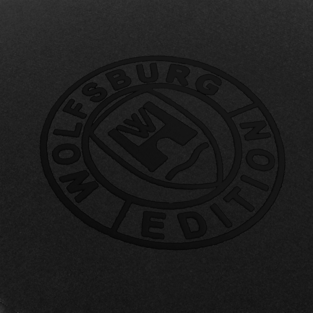 wob Detail-300 schwarz Das Wolfsburg Editions Logo auf einem schwarzen Teppich und das Logo ist in schwarz.