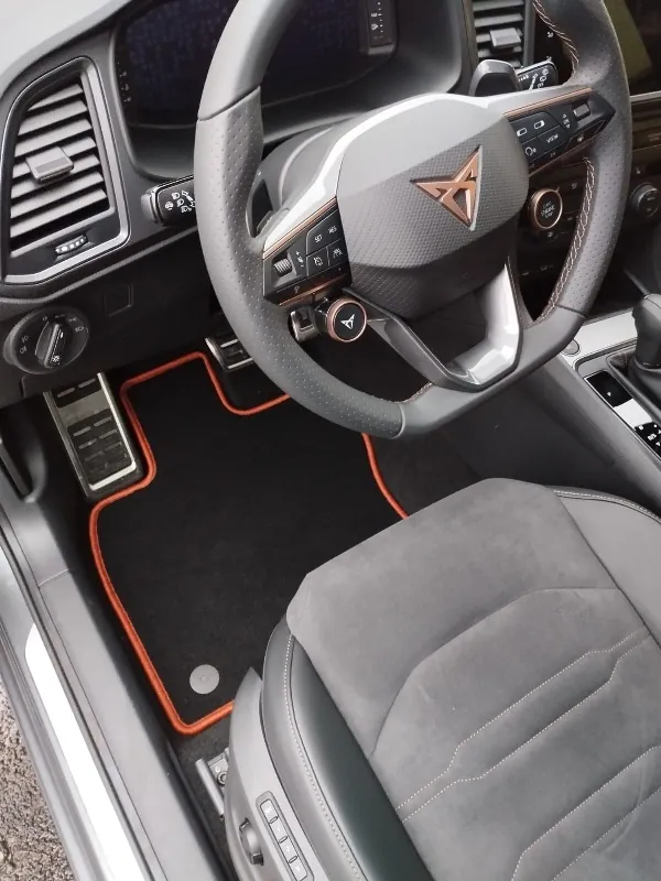 Blick in den Fahrerfußraum eines Cupra Ateca, in dem eine schwarze Fußmatte mit rotem Rand liegt.