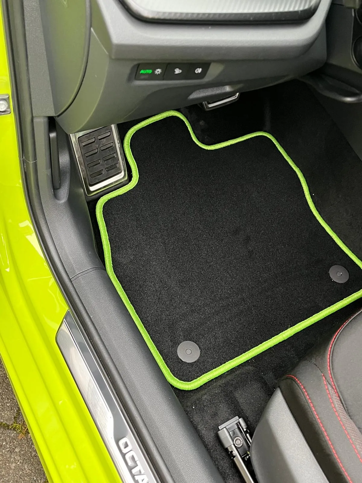 Blick in den Fahrerfußraum eines Skoda Octavia 4 RS, in dem eine schwarze Fußmatte mit neon-grünem Rand liegt