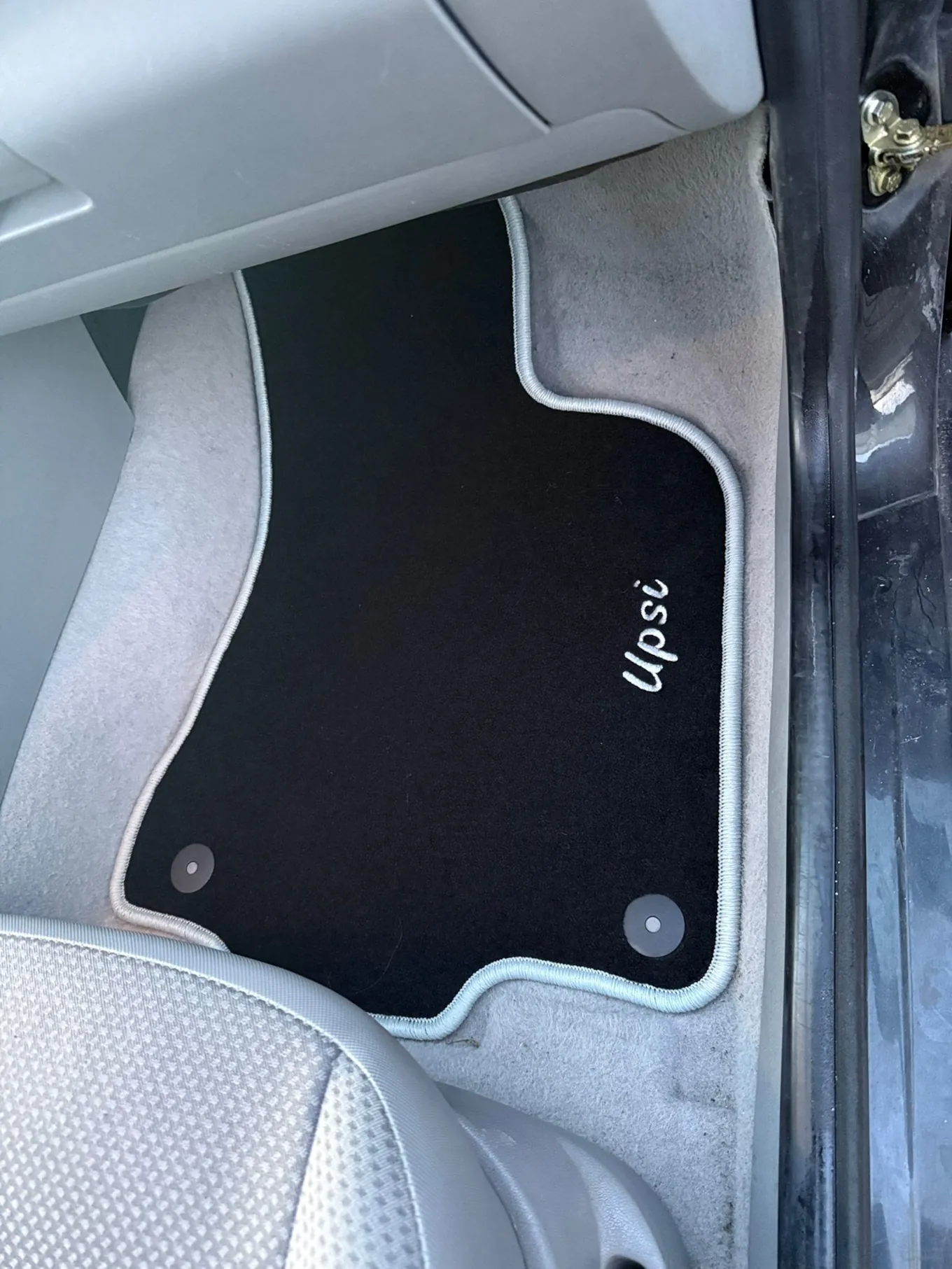 Blick in den Beifahrerfußraum eines VW Up, in dem eine schwarze Fußmatte mit der Bestichung „Upsi“ liegt