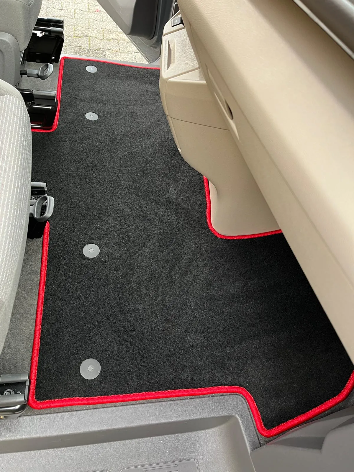 Blick in die Fahrerkabine eines VW T7 New Multivan 5, in der eine schwarze, perfekt eingepasste Fußbodenmatte mit rotem Rand liegt