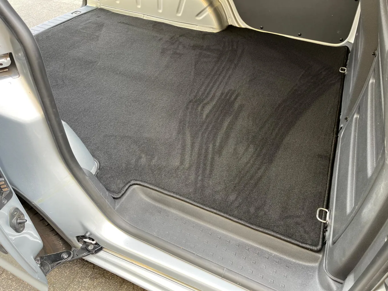 Blick durch die Seitentür in den Laderaum eines VW Caddy, dessen Boden mit einer schwarzen Laderaumschutzmatte verkleidet ist.